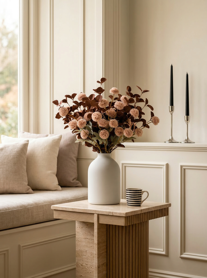 Decorative setup with a vase of flowers, candles, and a cup on a wooden table in a room with wainscoting.