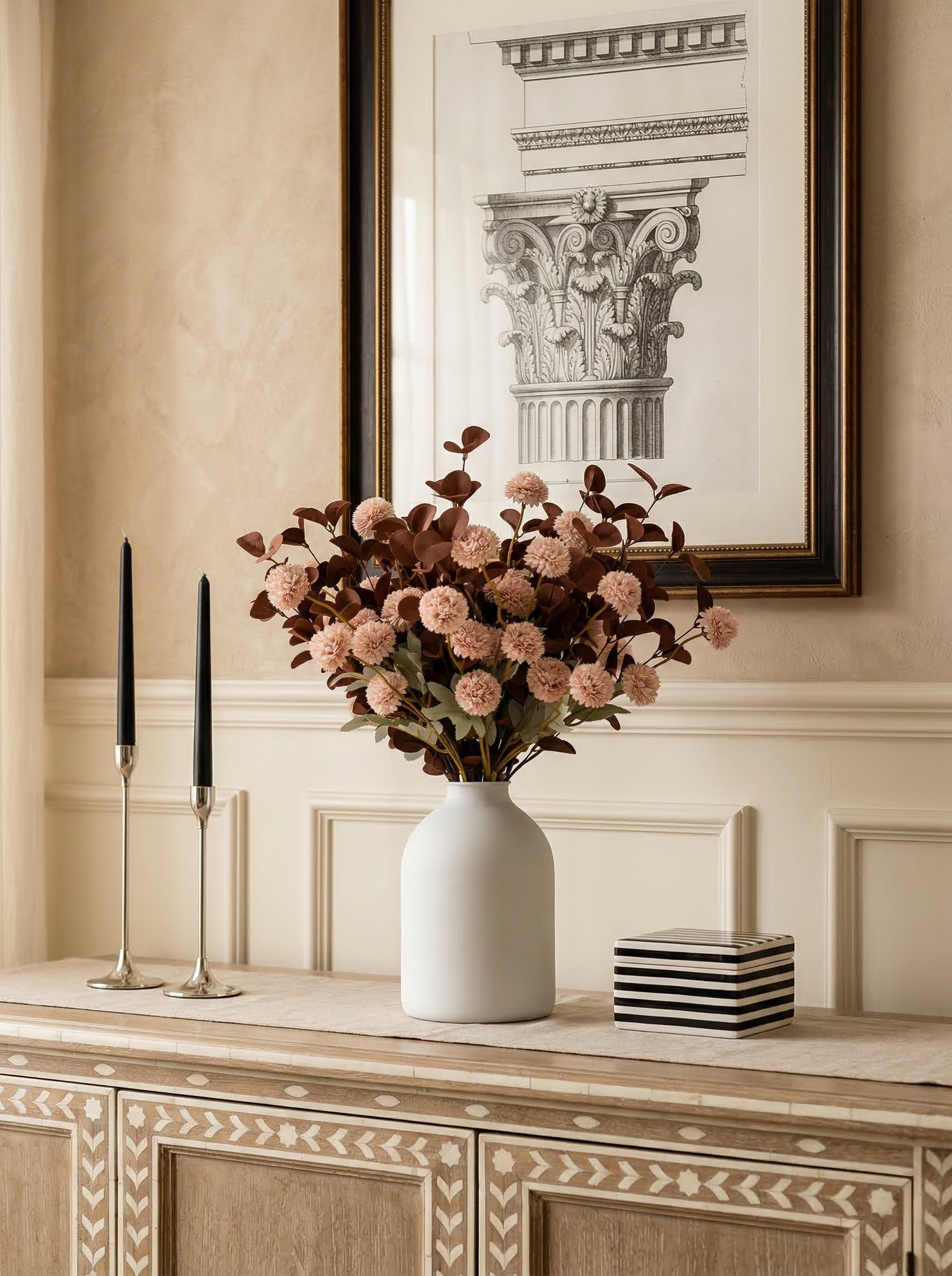 Decorative vase with flowers on a wooden console table against a wall with framed art.