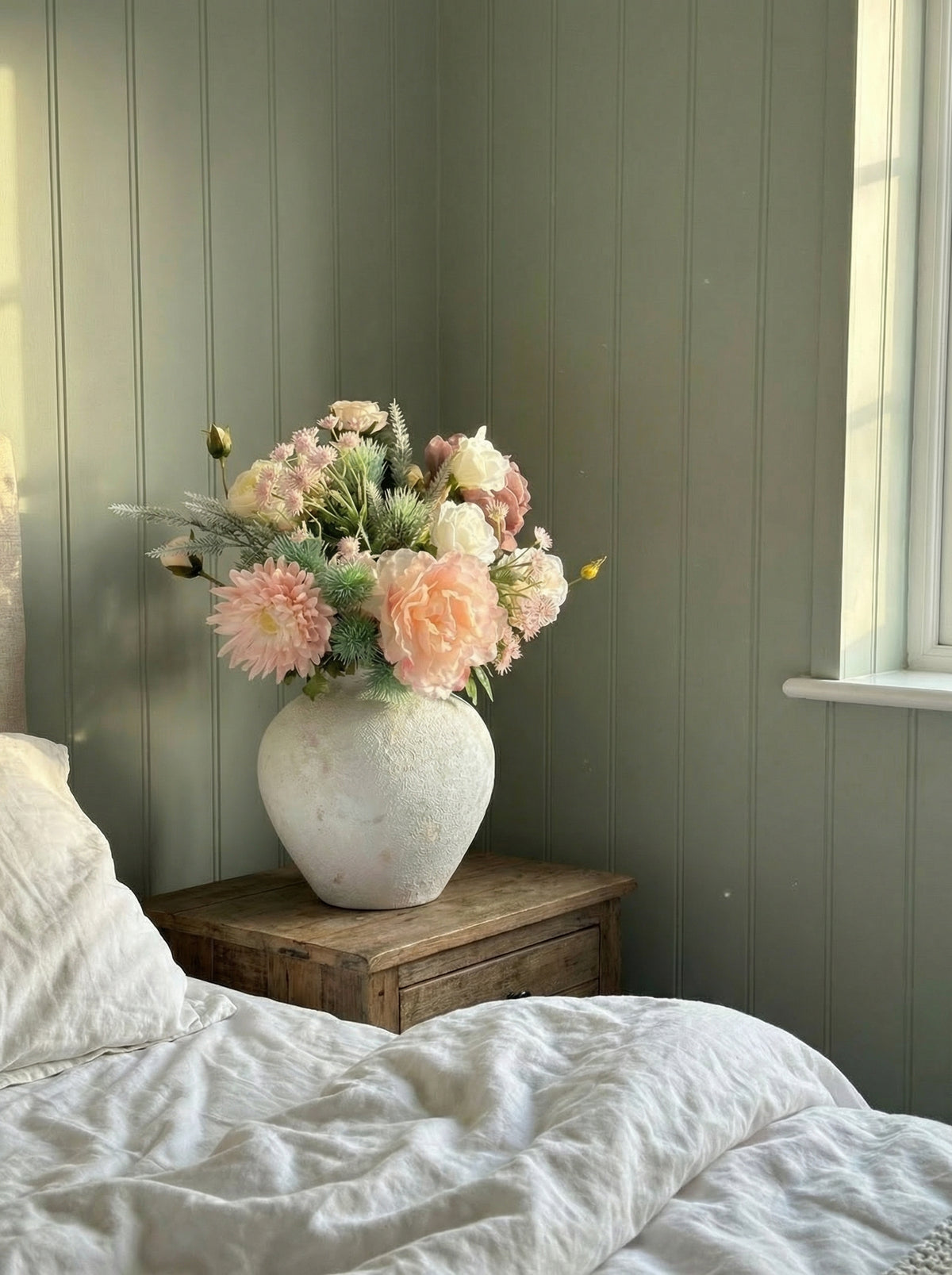 Floral arrangement in a vase on a wooden nightstand against a green paneled wall.