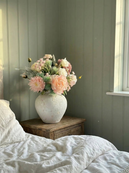 Floral arrangement in a vase on a wooden nightstand against a green paneled wall.
