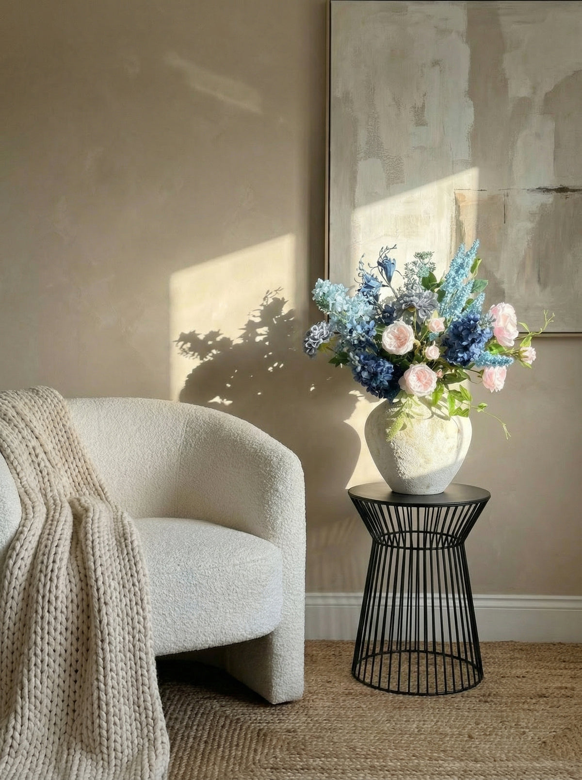 Floral arrangement in a white vase on a black wire side table next to a textured armchair.