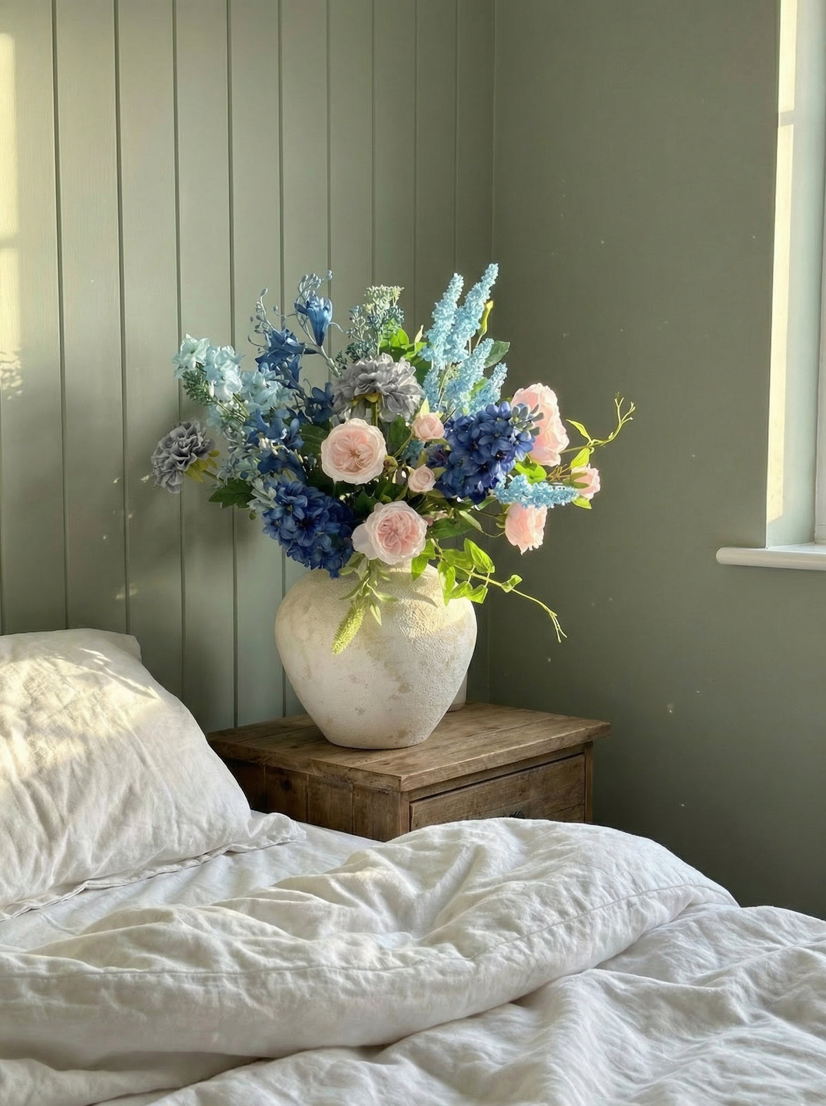 Vase of flowers on a bedside table with a bed in the foreground