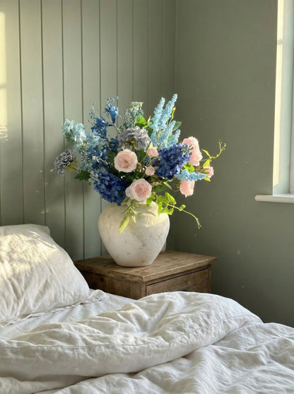 Vase of flowers on a bedside table with a bed in the foreground