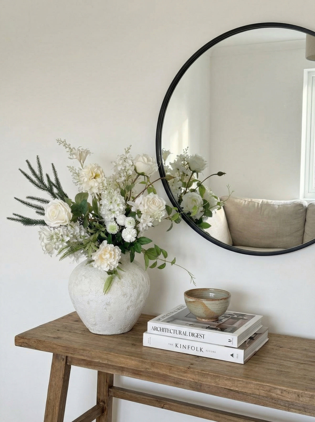Vase with flowers on a wooden table next to a round mirror