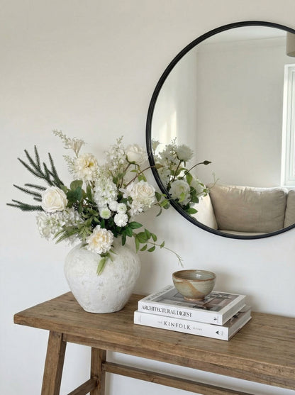 Vase with flowers on a wooden table next to a round mirror