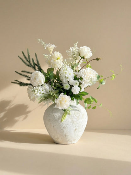 White floral arrangement in a textured white vase on a beige background