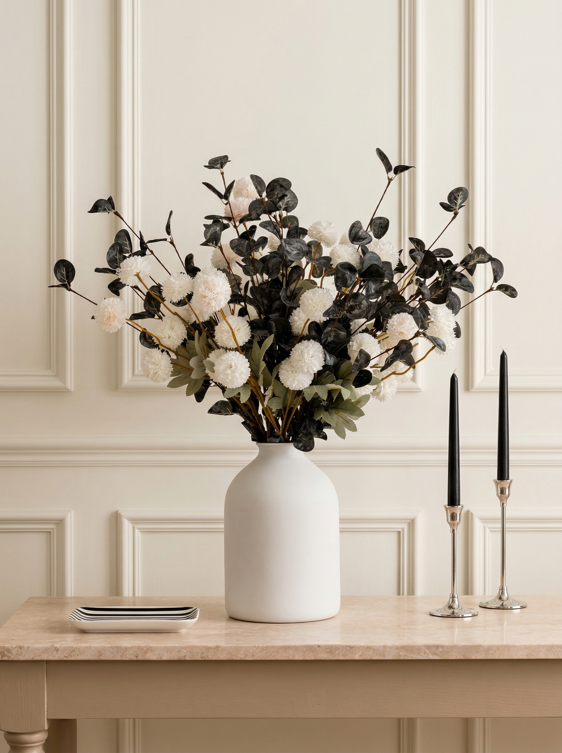 White vase with black and white floral arrangement on a table against a light-colored wall.