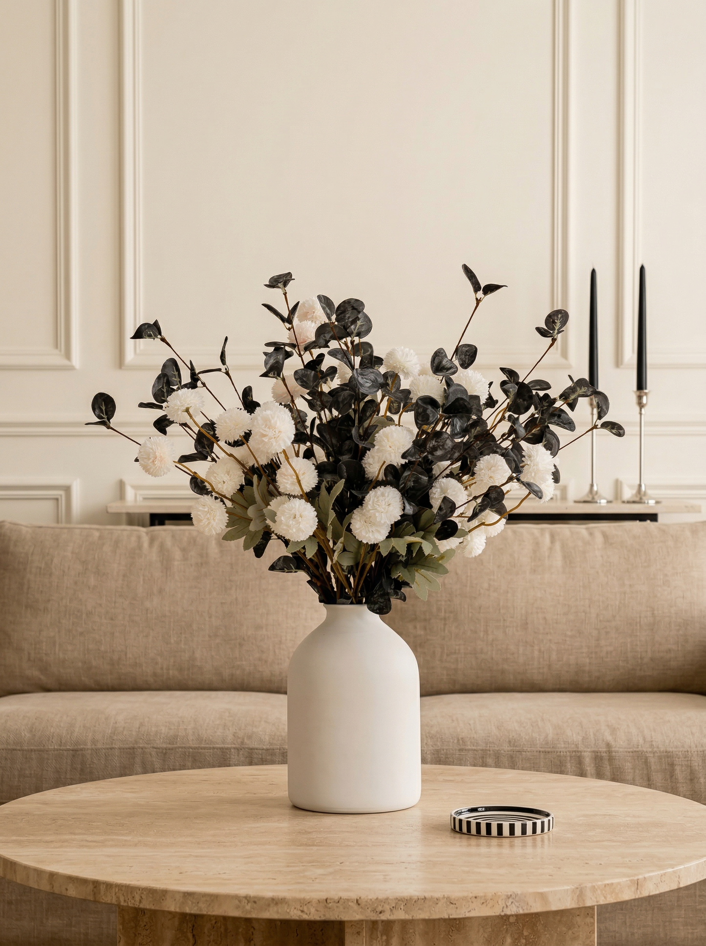 White vase with black and white floral arrangement on a wooden table in a living room.