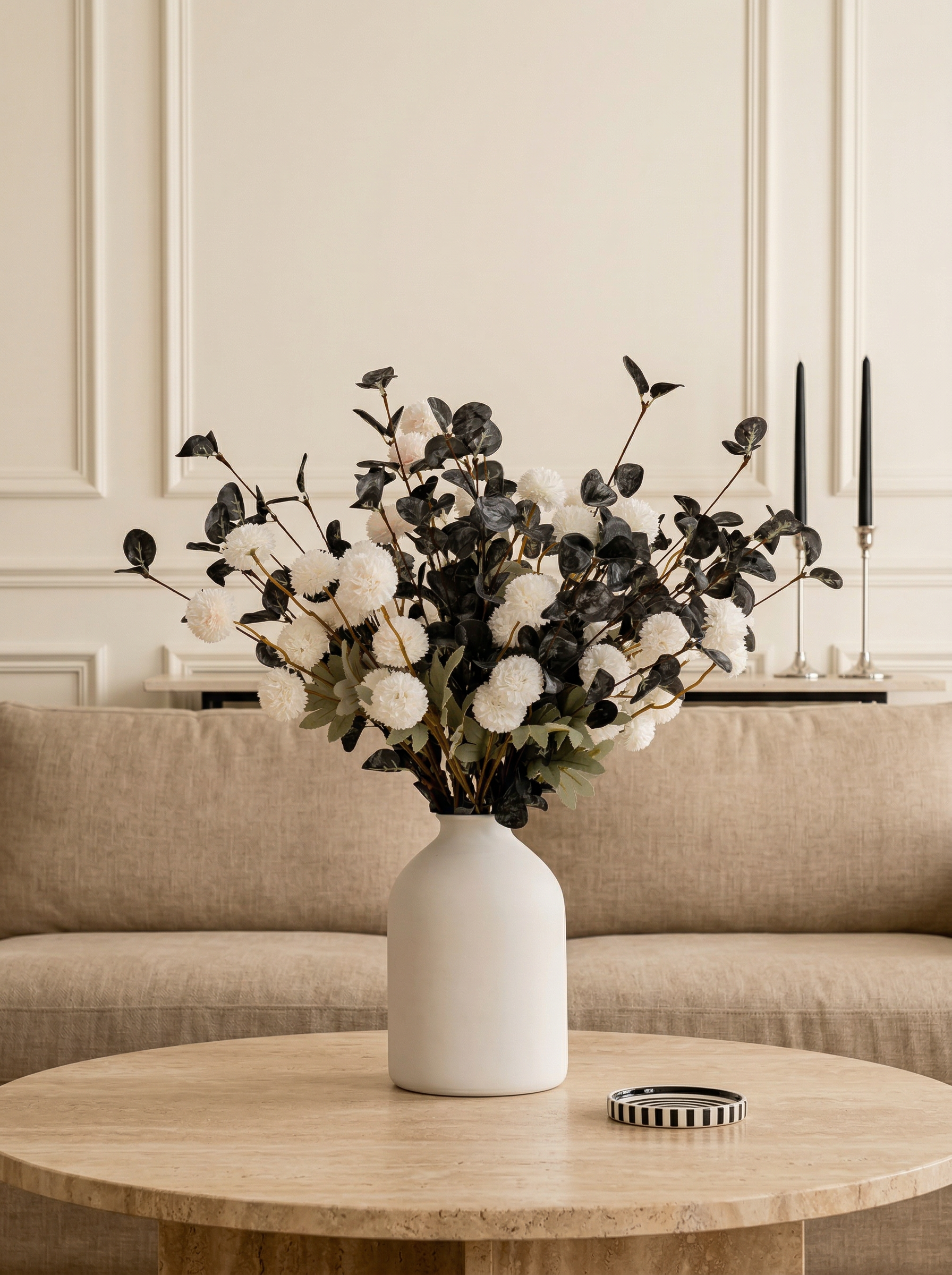 White vase with black and white floral arrangement on a wooden table in a living room.