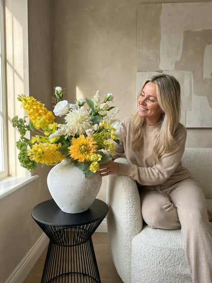Woman sitting on a couch with a large vase of flowers on a side table.