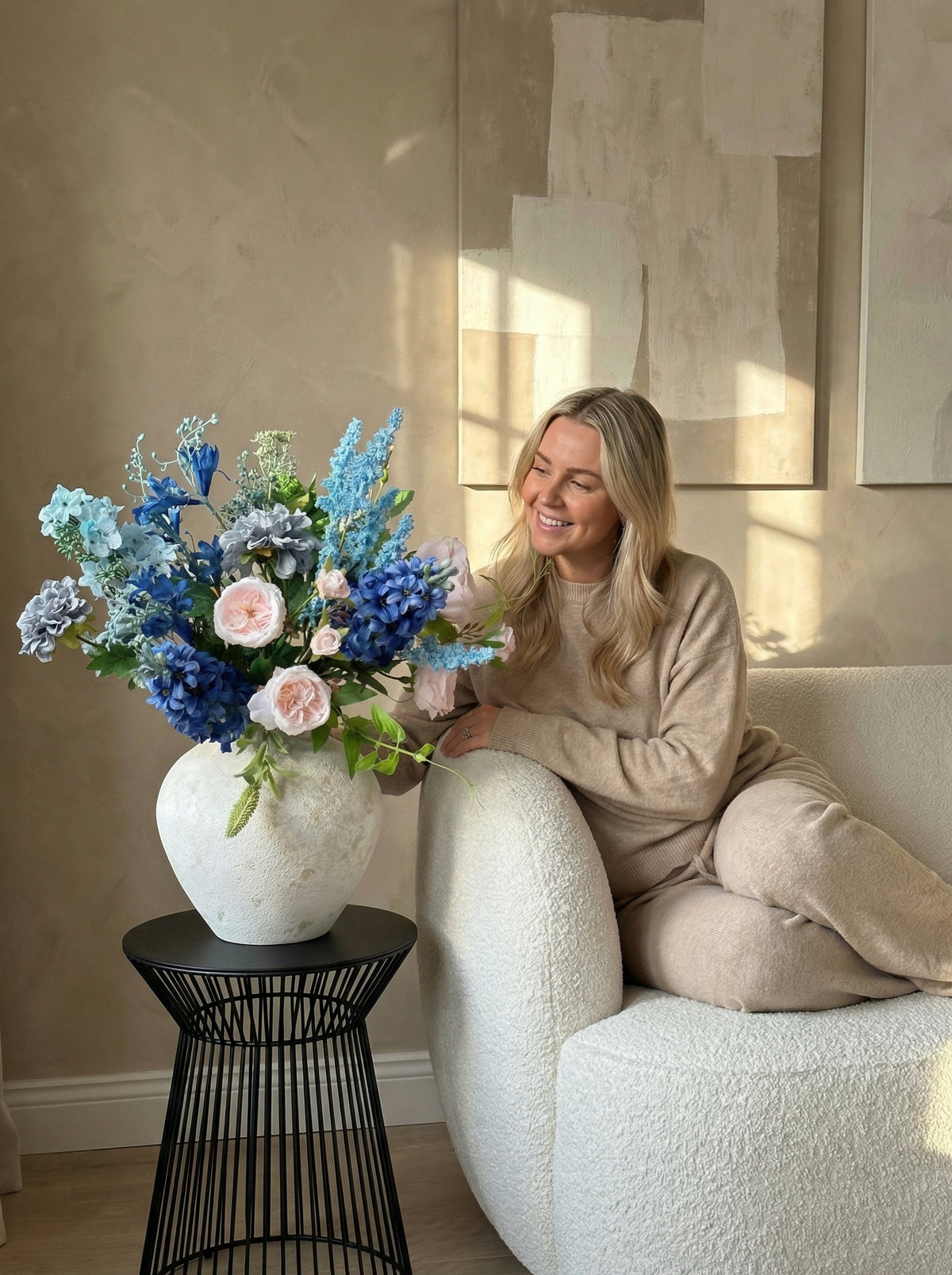 Woman sitting on a couch with a large vase of flowers on a side table.