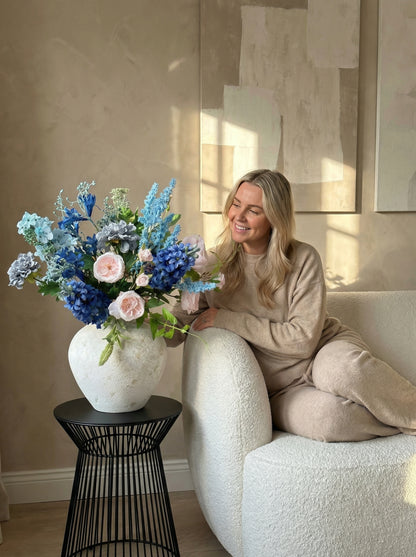 Woman sitting on a couch with a large vase of flowers on a side table.